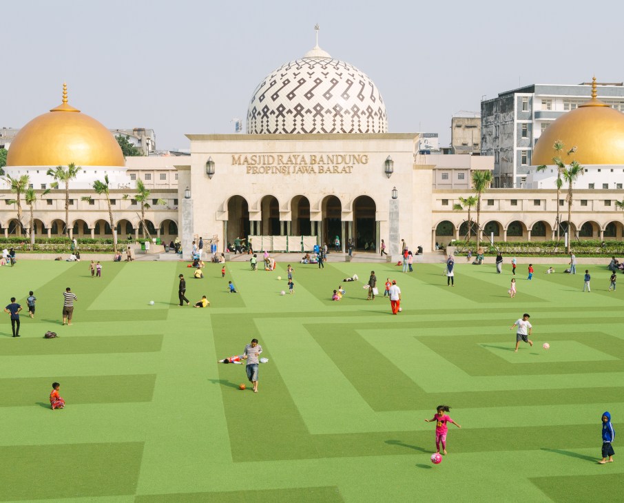 Families play and relax on green Astroturf at Alun-Alun Park with Bandung's Grand Mosque behind.
