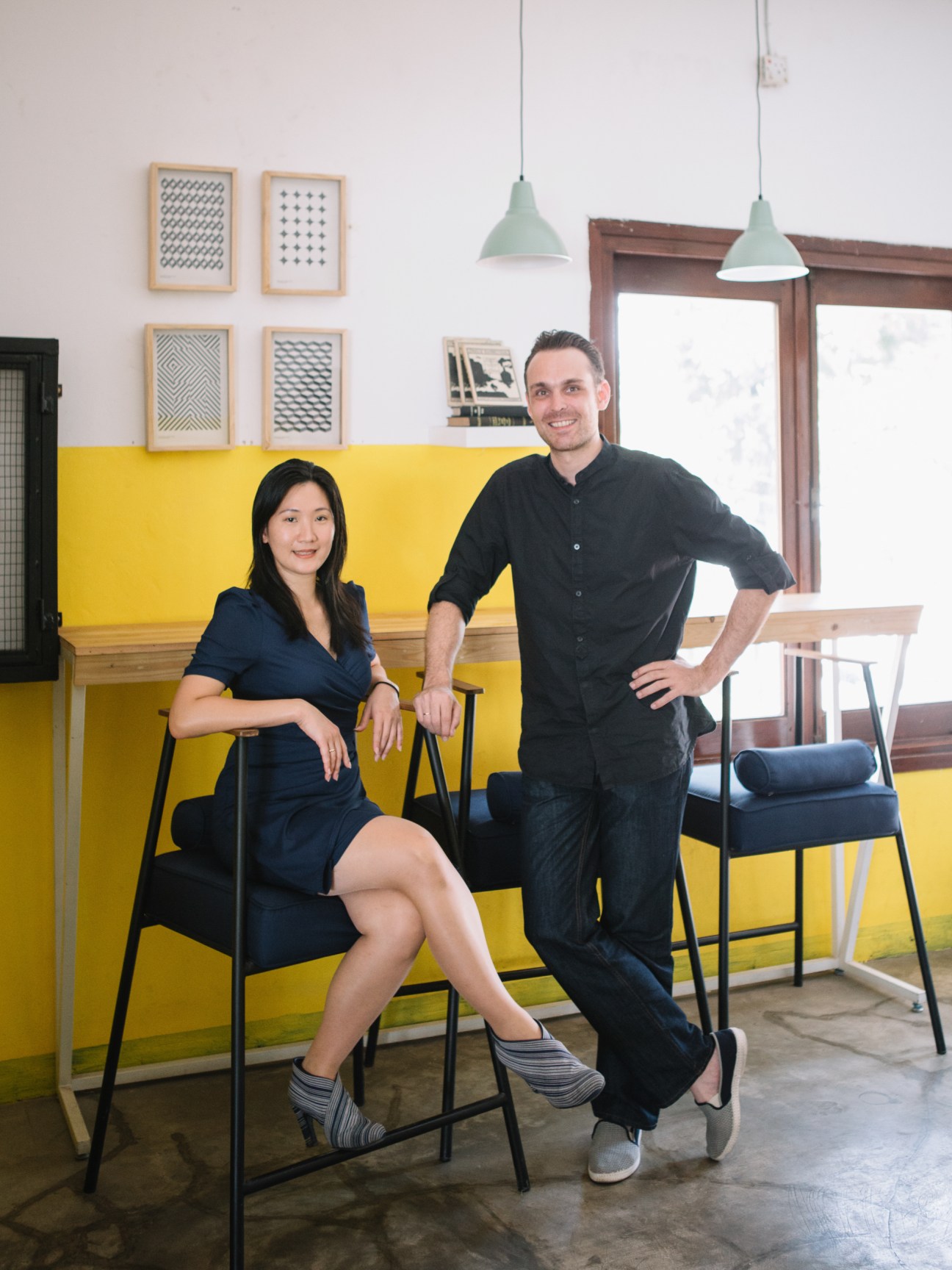 Daliana Suryawinata and Florian Heinzelmann of Shau architects pose in their office with yellow wall paneling.