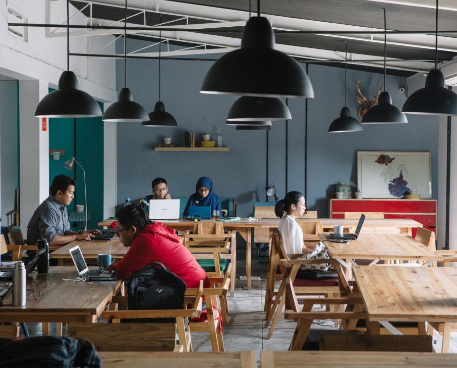 Shau architects office with wooden desks, black pendant lights, and staff working at laptops.