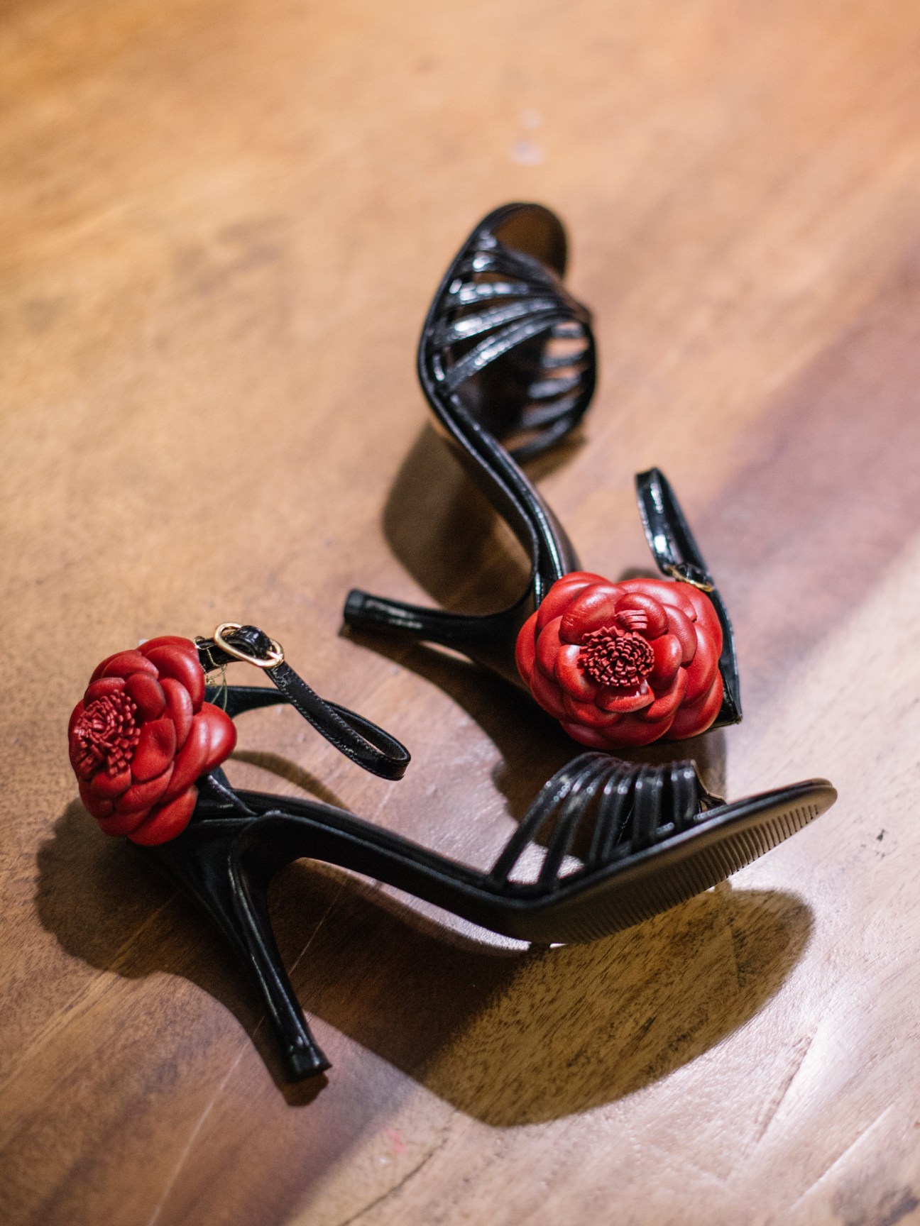 Black tango shoes with red flower appliqués and curved heels displayed on a wooden surface.