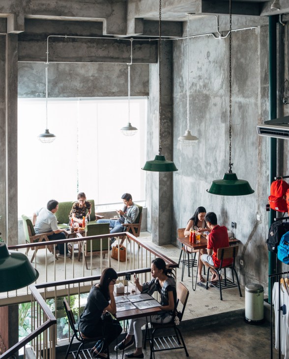 Interior of ORE clothing store and café with customers seated at tables under pendant lamps in a multi-level concrete space.