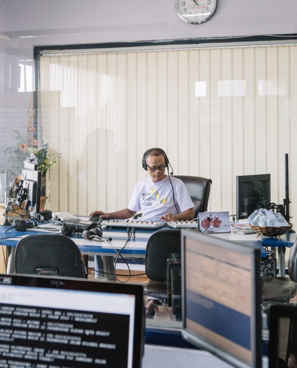 Radio presenter at Suara Surabaya station wearing headphones at broadcasting desk with equipment.