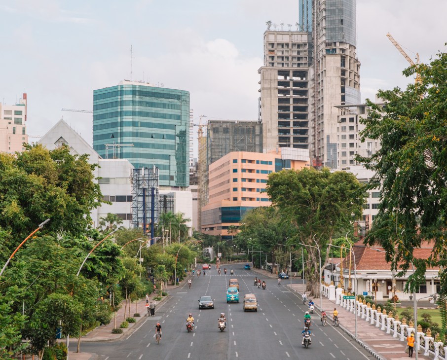 Street view of central Surabaya with modern high-rise buildings, green trees, and traffic on a wide boulevard.