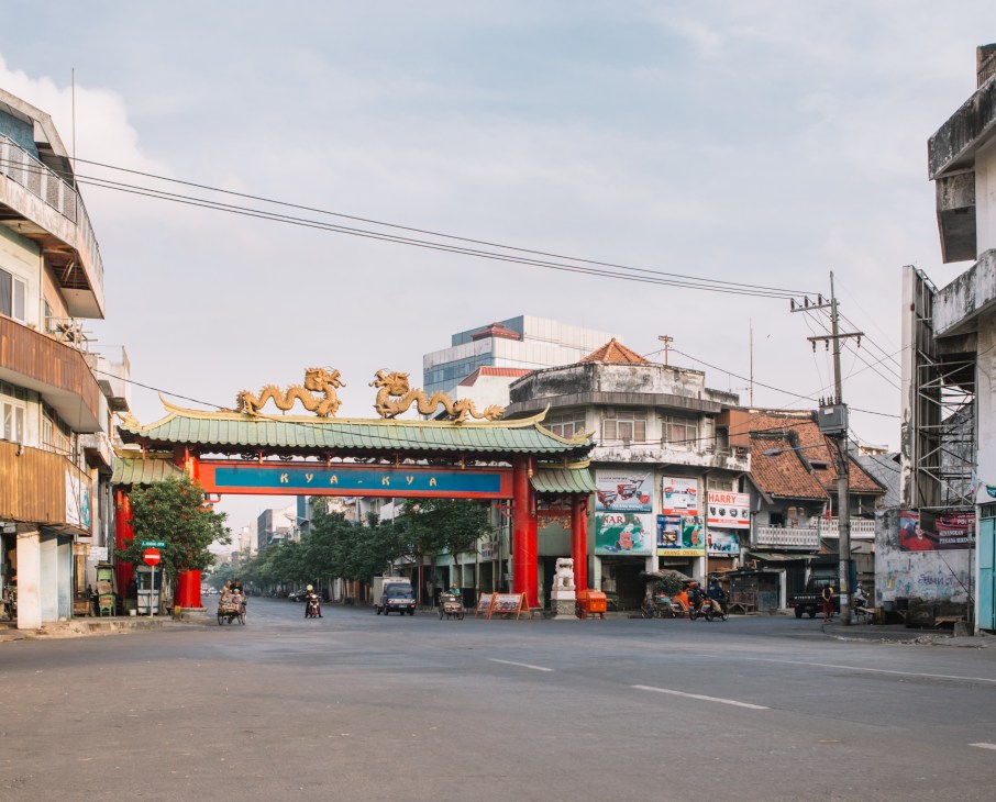 Ornate red and green gateway with golden dragons in Surabaya's Chinese quarter, flanked by colonial and modern buildings.