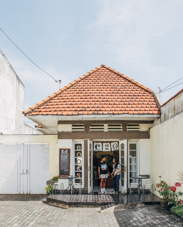 Entrance to C20 Library & Collabtive, a small cream-colored building with terracotta roof tiles and signage, with people visible inside.