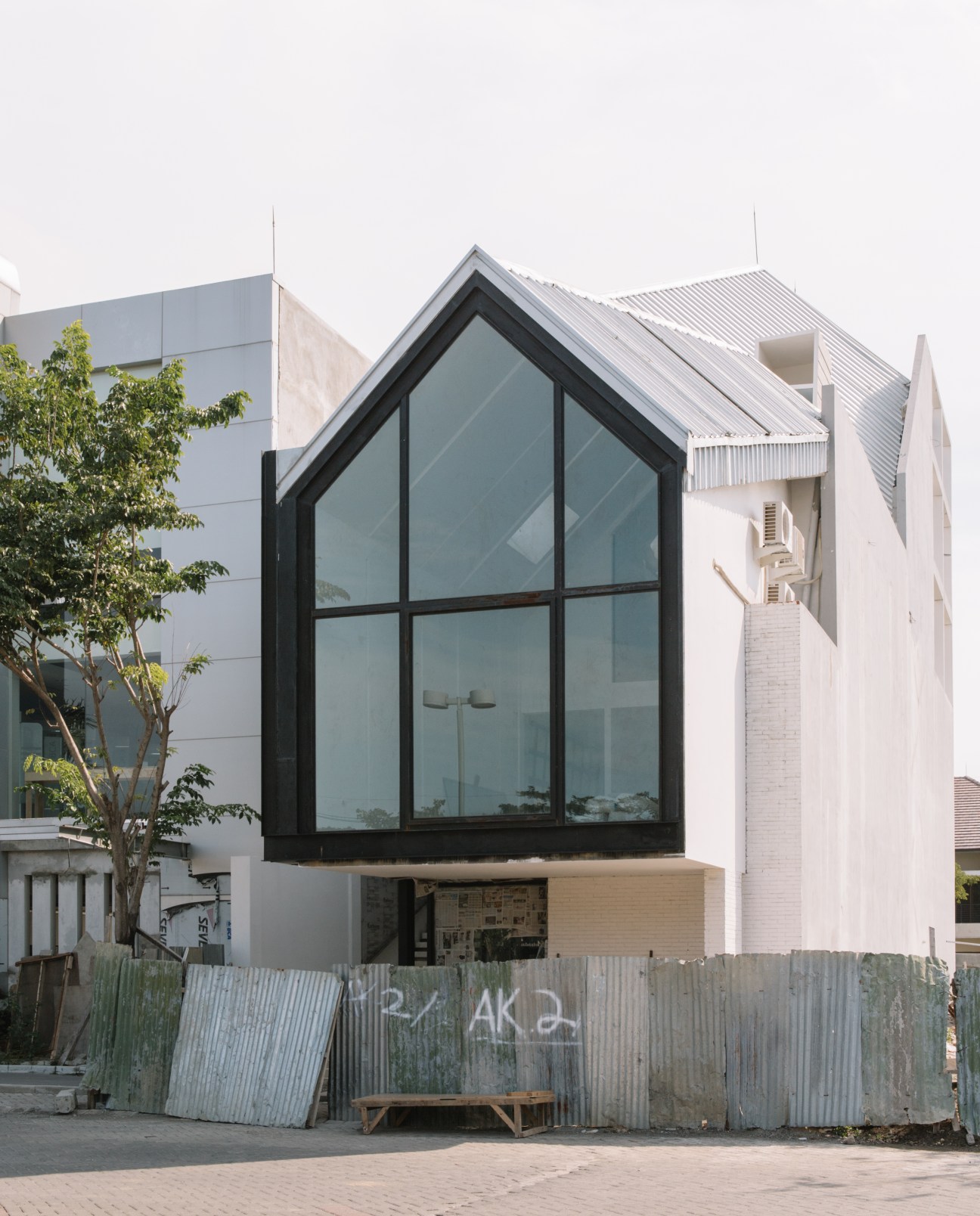 Modern house with large black-framed windows and white walls next to older Dutch colonial architecture in Surabaya