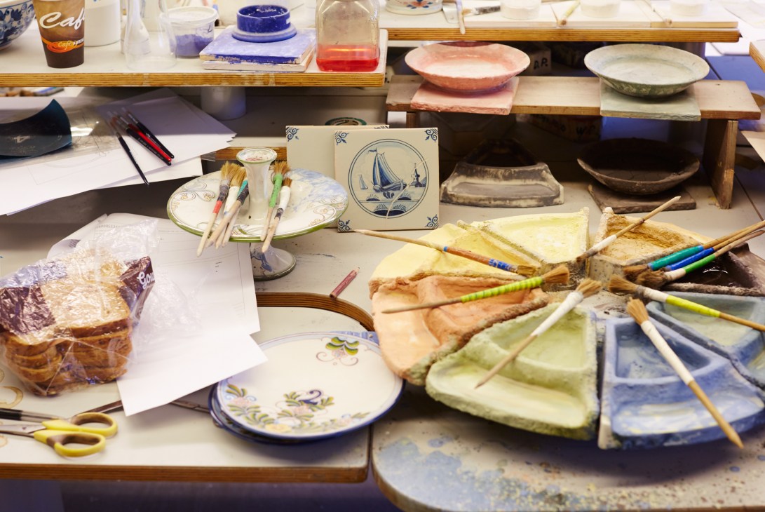 Royal Tichelaar decorating department with artisans handpainting ceramic tiles and plates with traditional blue and floral patterns.