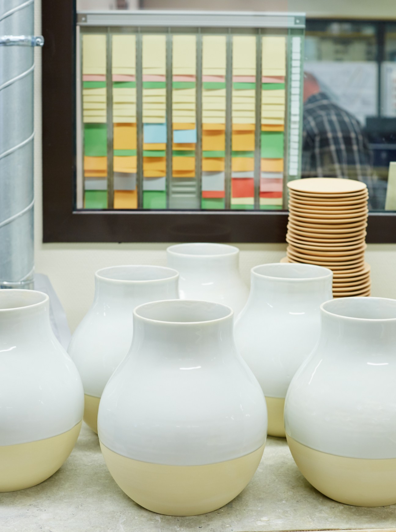 White and cream glazed ceramic vases displayed with stacked wooden plates against a colorful tile sample board.