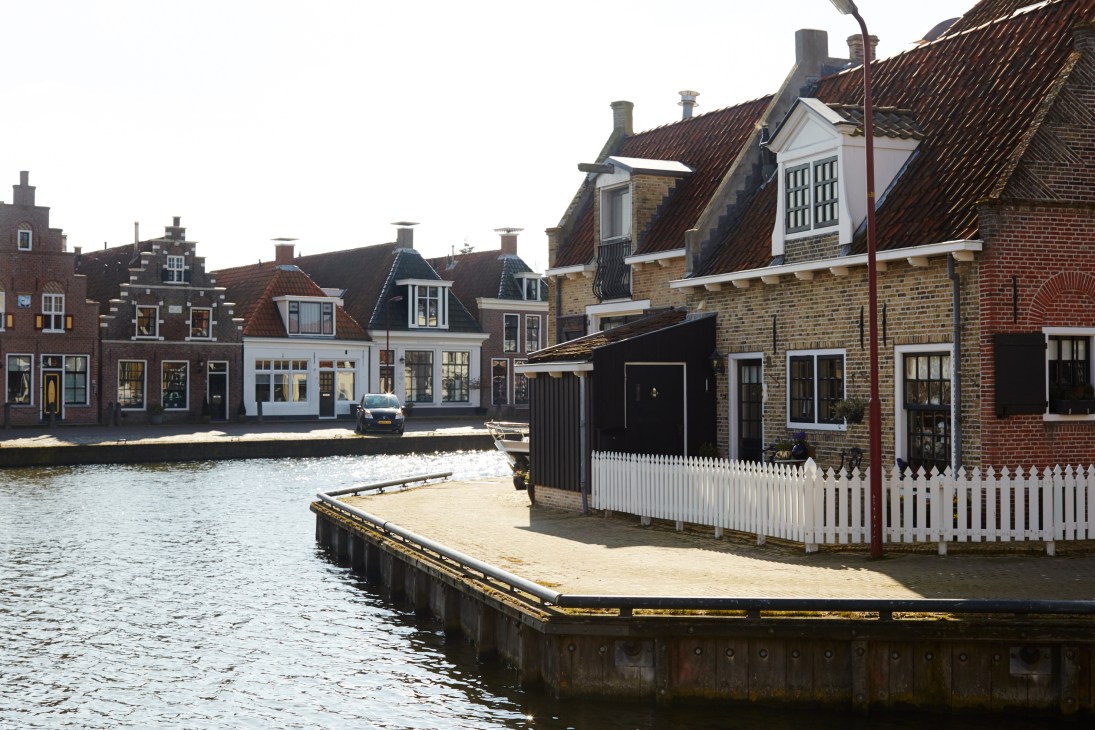 Traditional Dutch brick houses with tiled roofs line a waterfront canal in Makkum village.