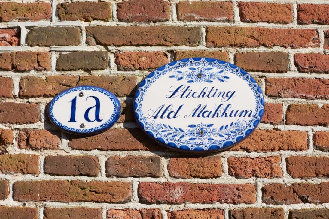 Blue and white ceramic house number and nameplate reading '1a' and 'Stichting Ald Makkum' mounted on a brick wall.