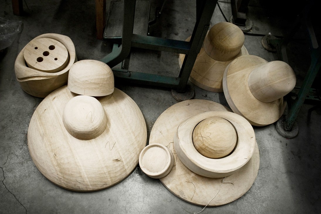 Wooden hat-shaping blocks of various sizes arranged on a workshop floor.