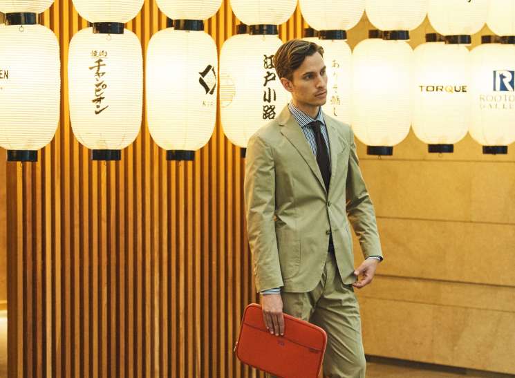 Man in tailored suit and laptop case standing at Tokyo International Airport.
