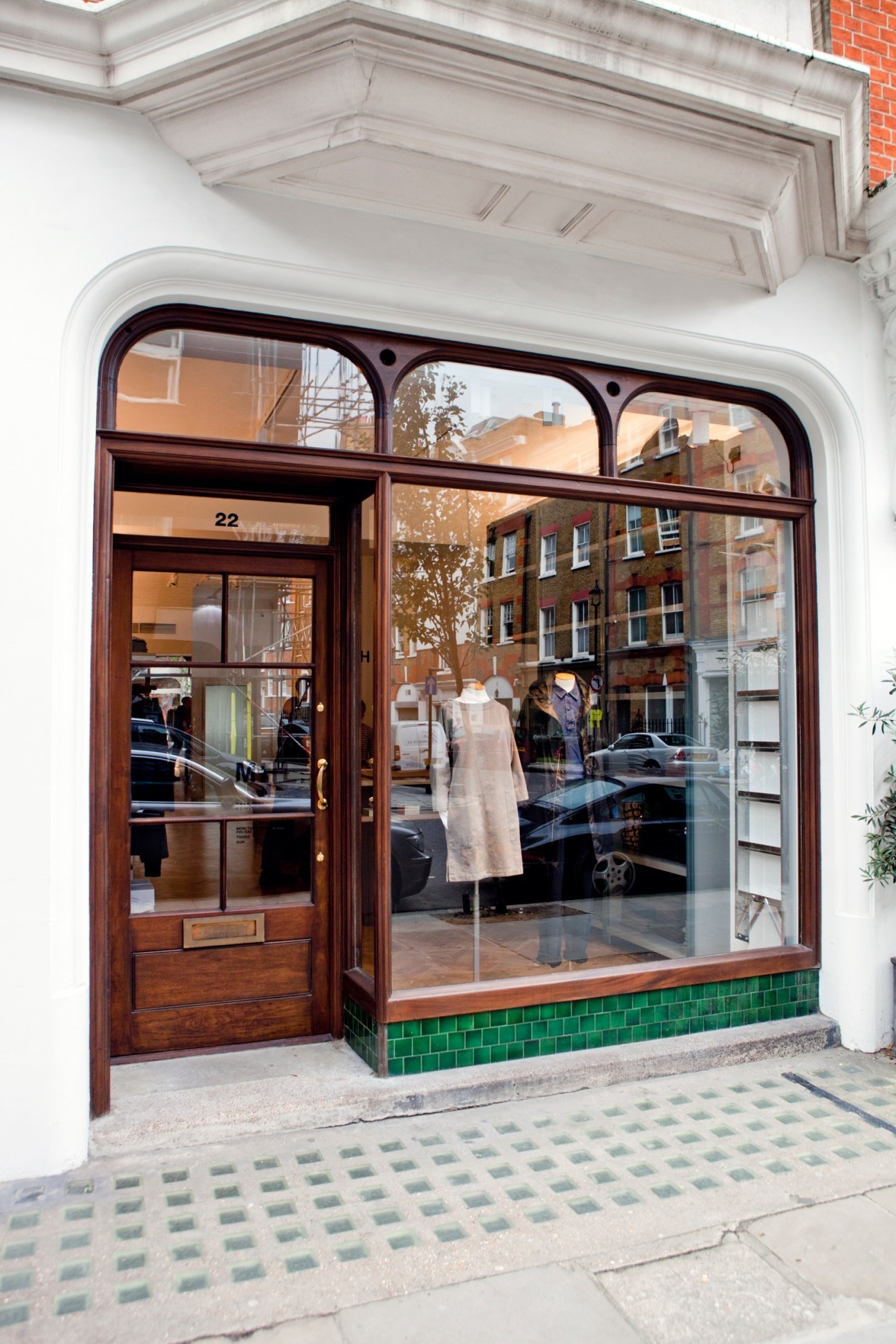 Margaret Howell storefront with wooden frame, green tile base and cream garment on display mannequin.