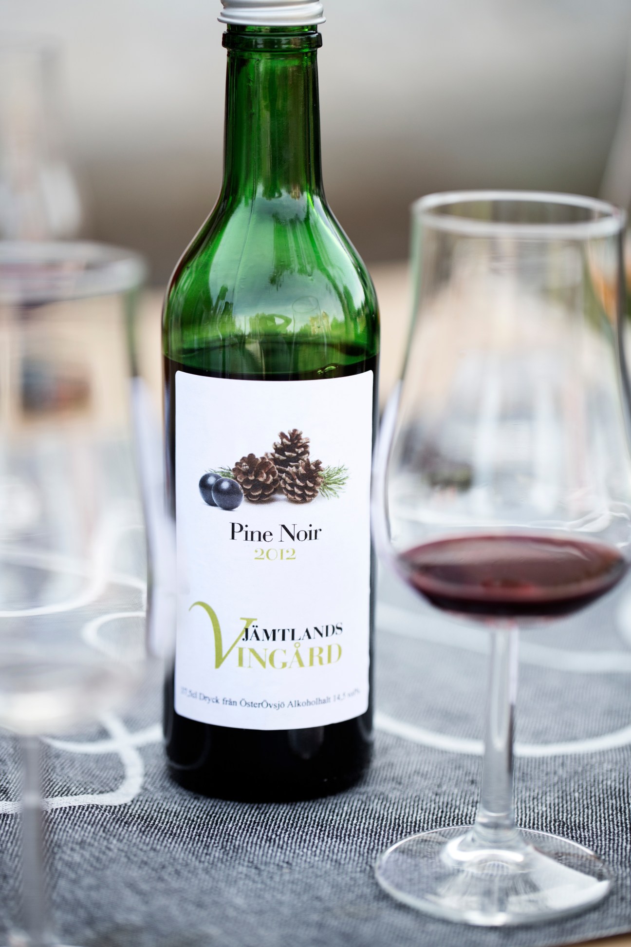 Bottle of Pine Noir 2012 from Jämtlands Vingård with a glass of dark wine on a table.