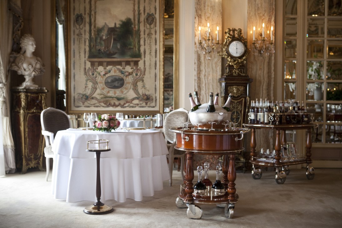 Elegant dining room at Le Louis XV with round table, wine coolers, and ornate classical decor.