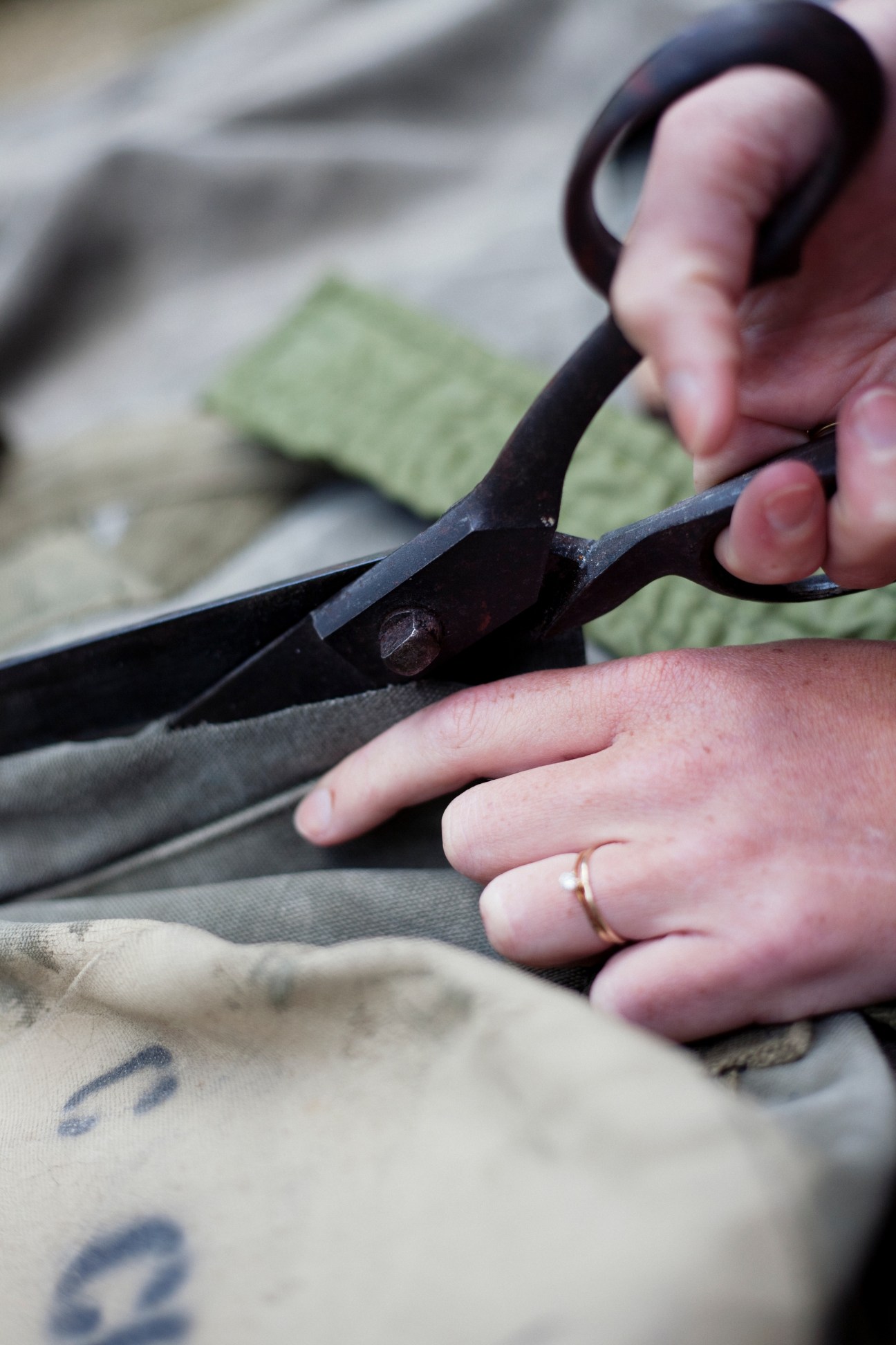 Hands holding black scissors cutting through numbered military fabric with printed markings.