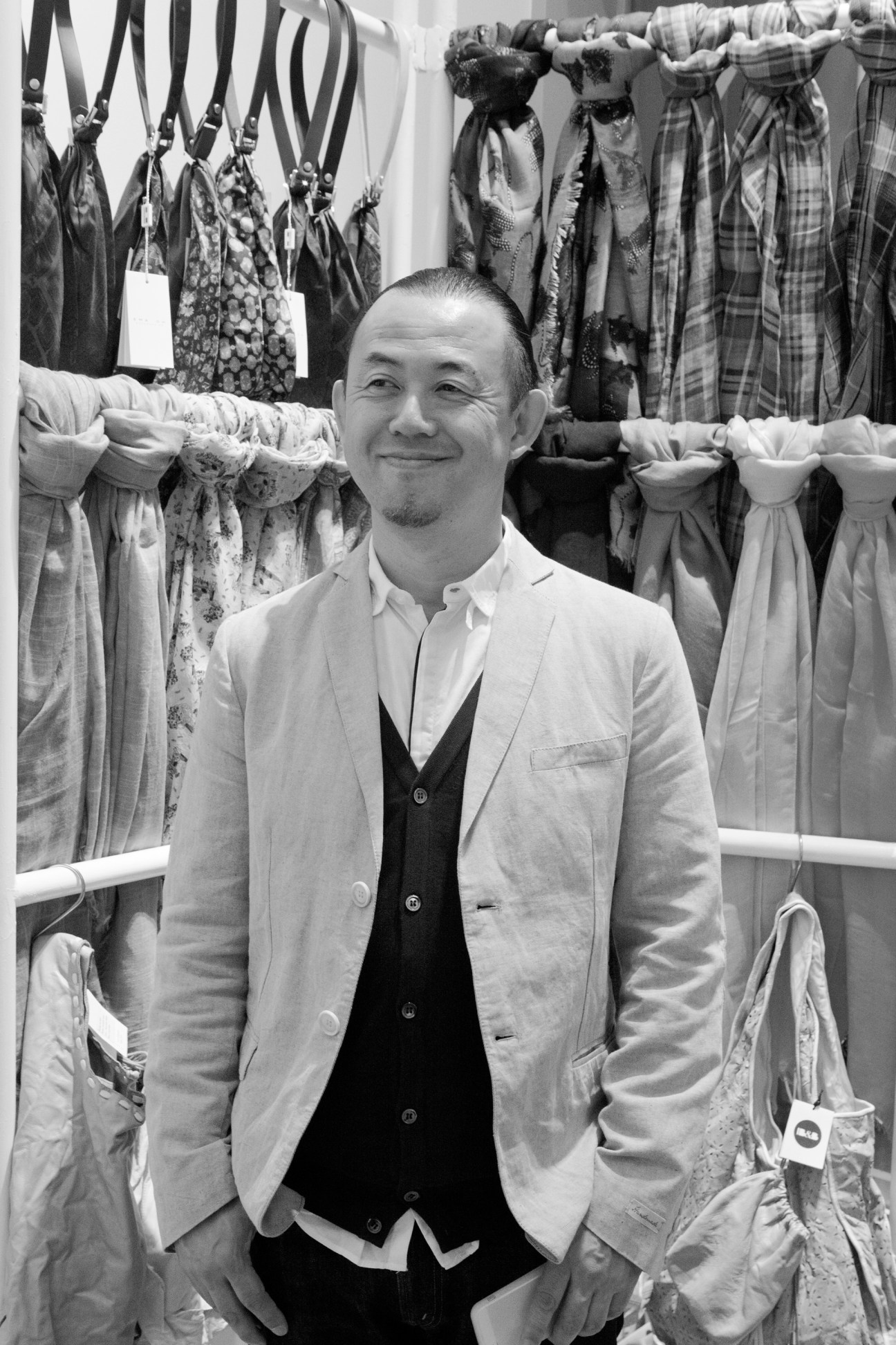 Mimio Sasaki stands in his store surrounded by hanging fabrics and scarves in various patterns and colors.