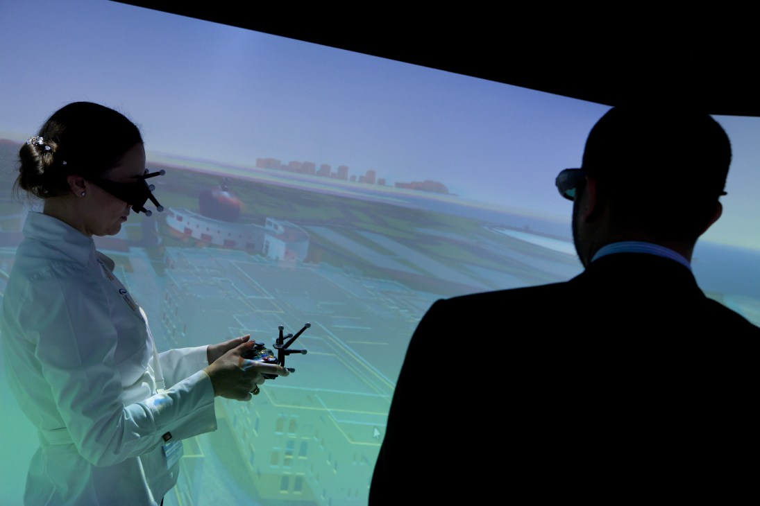 Woman in white blazer demonstrating a drone to two men viewing an aerial projection display at MIPIM.
