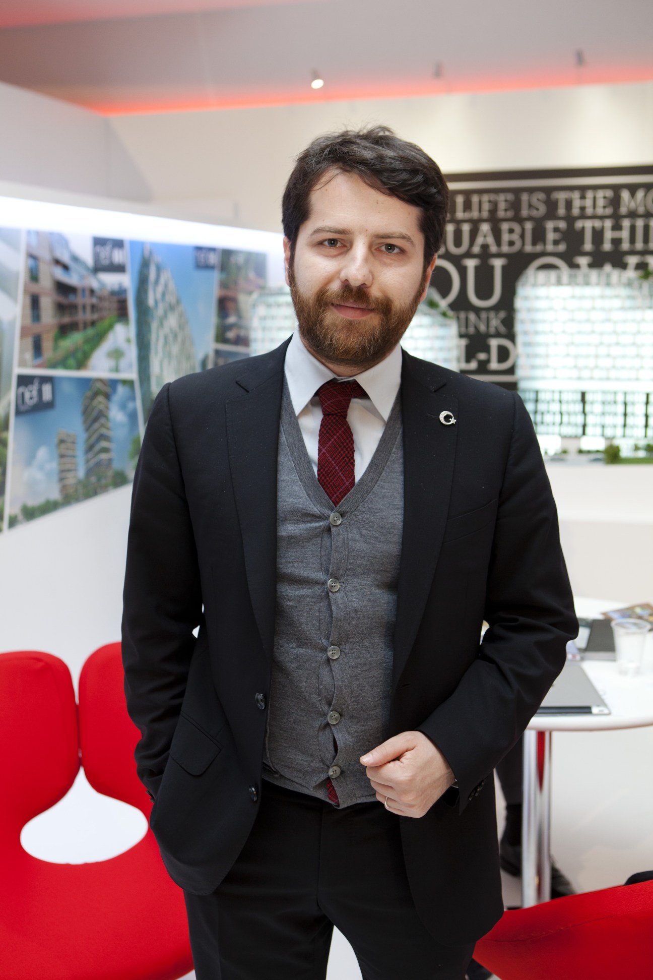 Erden Timur, founder of real estate lab NEF, stands at a MIPIM exhibition booth with architectural renderings displayed behind him.