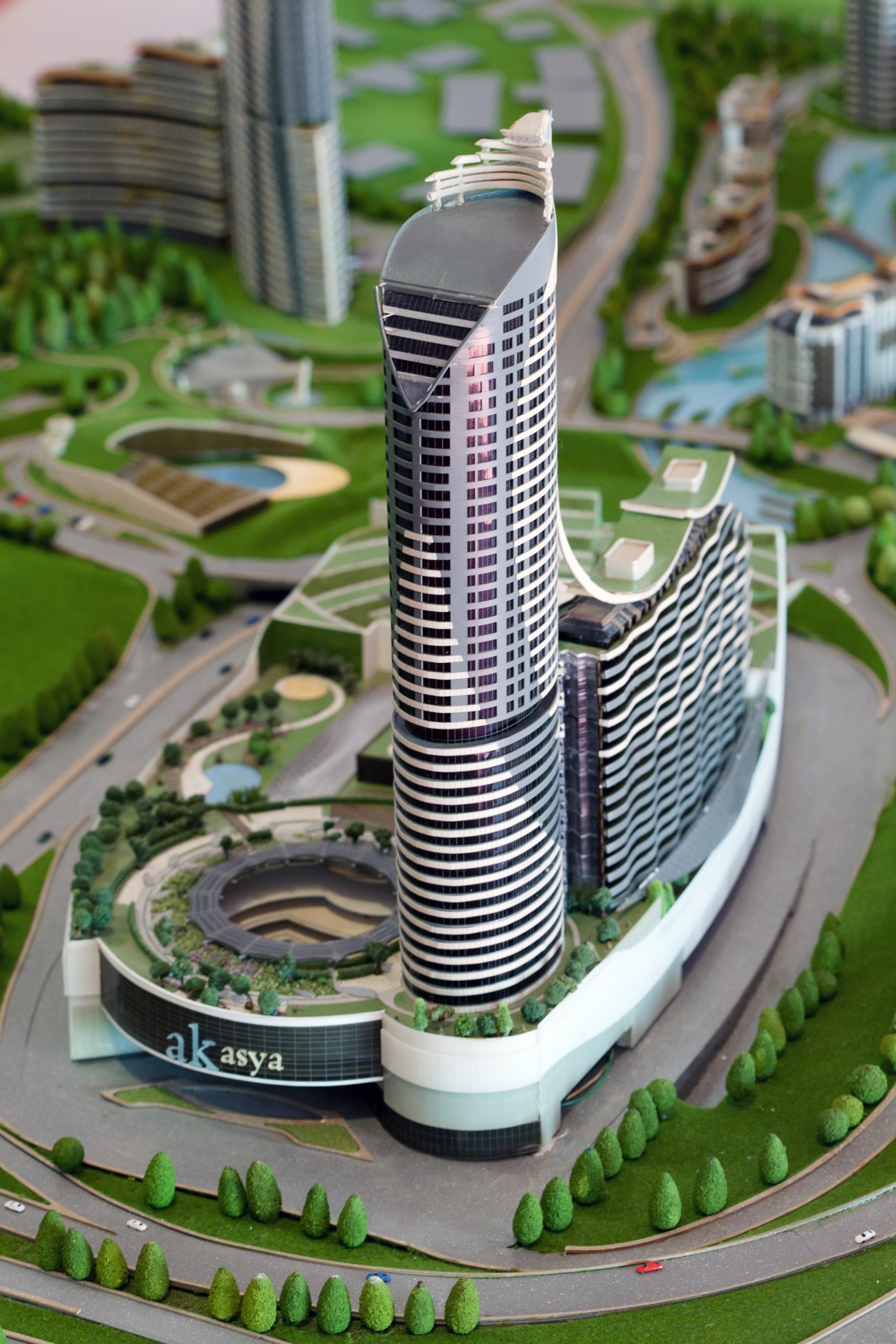 Architectural model of a spiraling high-rise residential tower with black and white striped facade labeled Akasaya, surrounded by landscaped grounds.