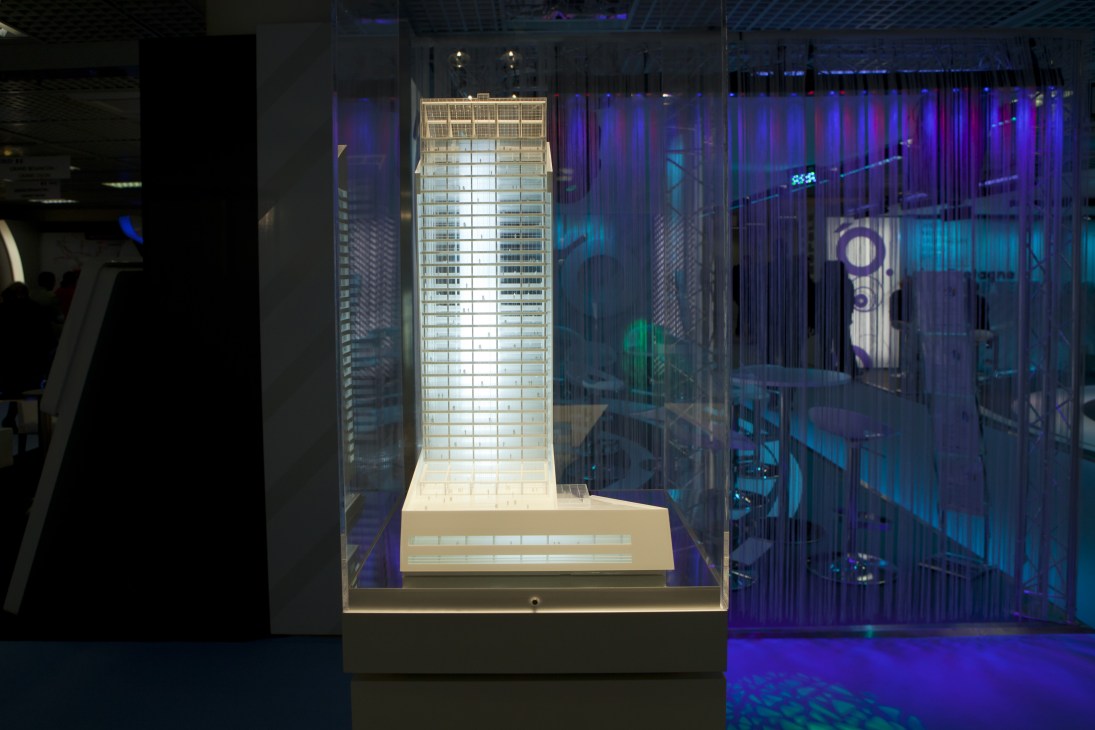 Illuminated architectural model of a tall residential tower displayed in a glass case at MIPIM