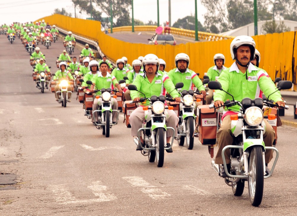 Mexican postal service workers in bright lime green and pink uniforms riding motorcycles in a large group parade.