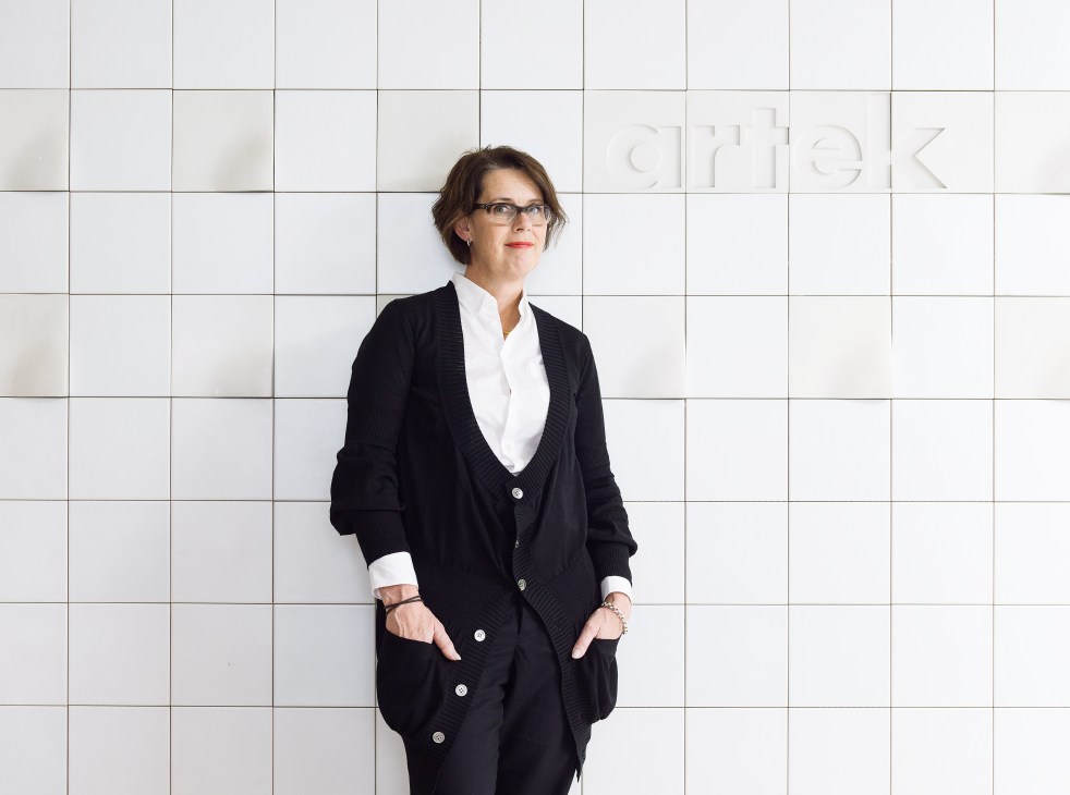 Mirkku Kullberg, CEO of Artek, stands against a white tiled wall wearing glasses and a black cardigan.