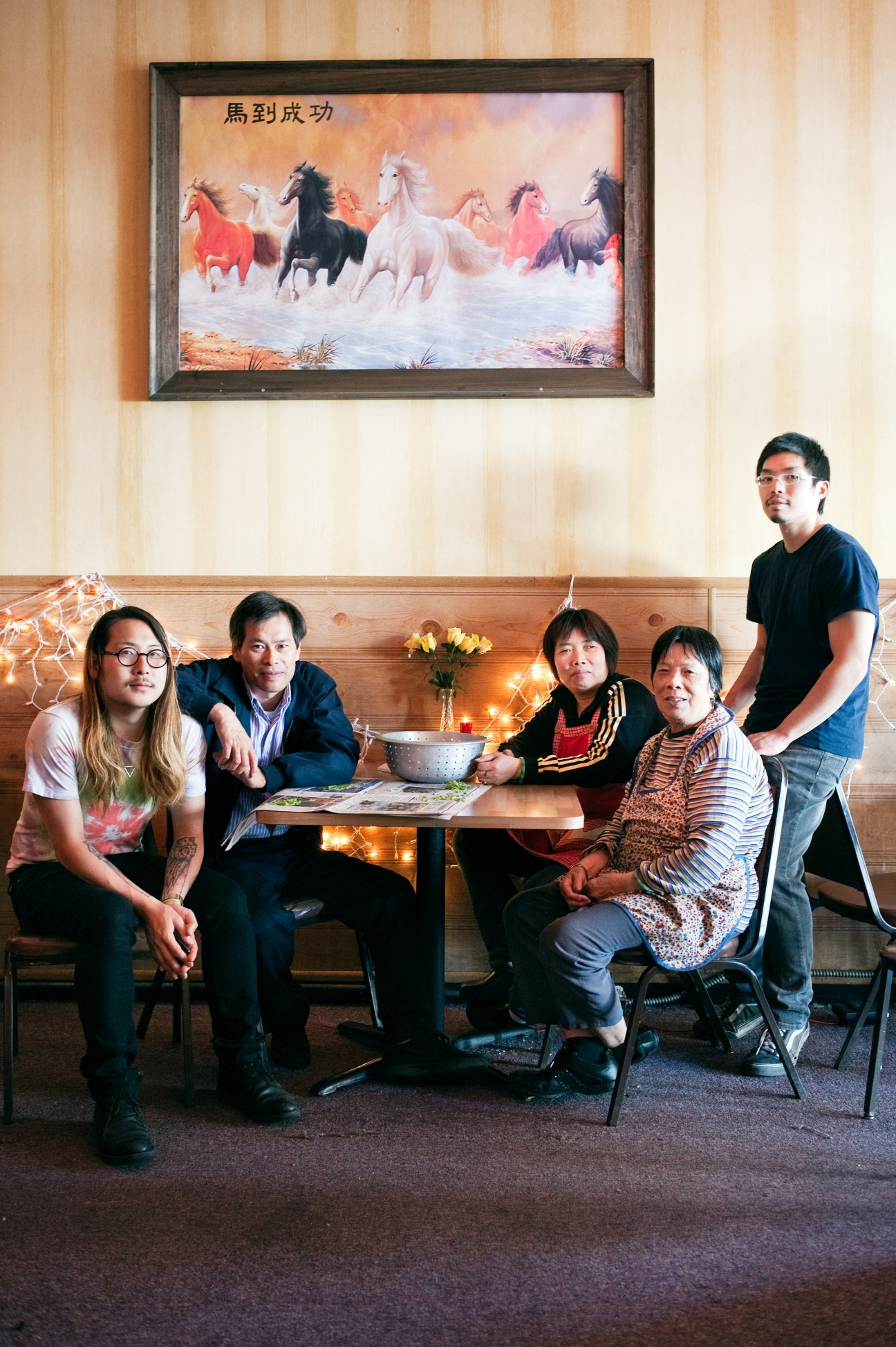 A group of five people pose together in a restaurant interior with wooden paneling and a framed artwork of horses on the wall above them.