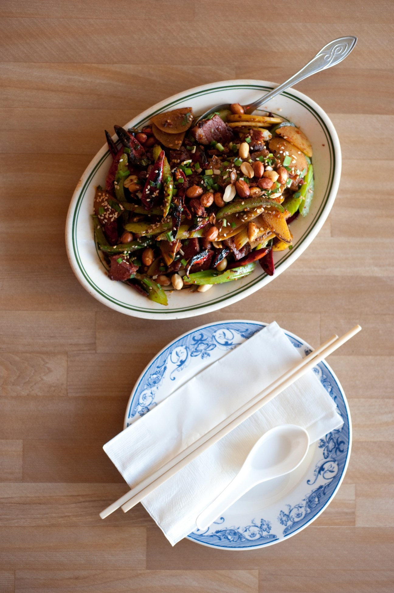 Overhead view of colorful Asian noodle dish with vegetables and peanuts in a white bowl with decorative spoon.
