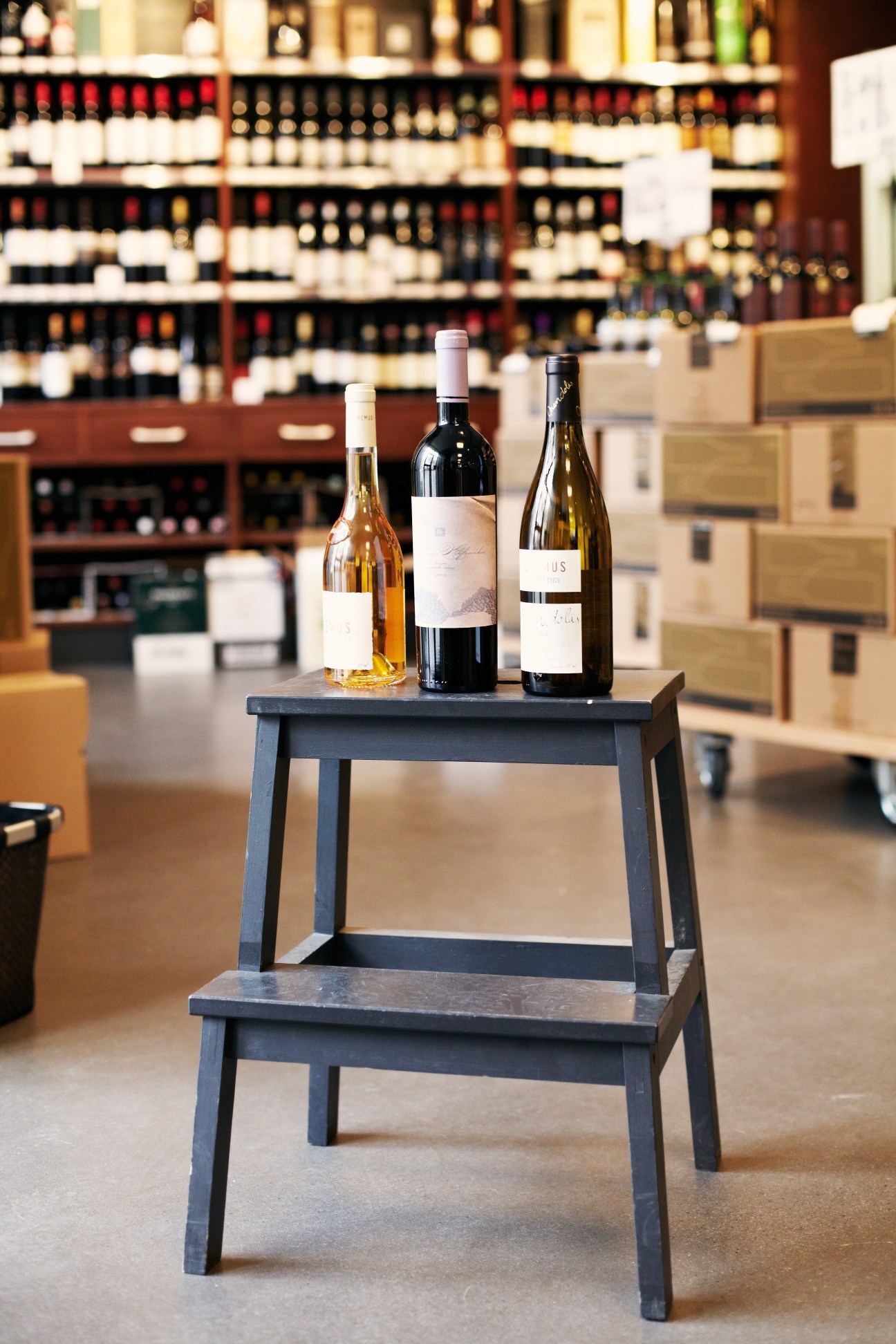 Three Hungarian wine bottles displayed on a dark wooden table in a wine shop with shelves of wines in the background.