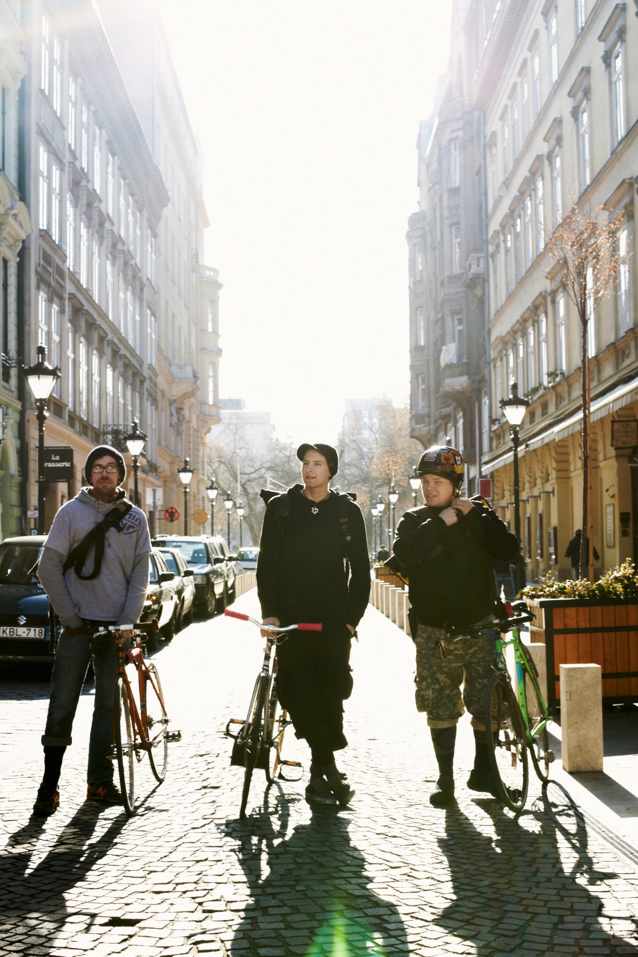Three couriers with bicycles standing on a cobblestone street lined with historic European buildings.
