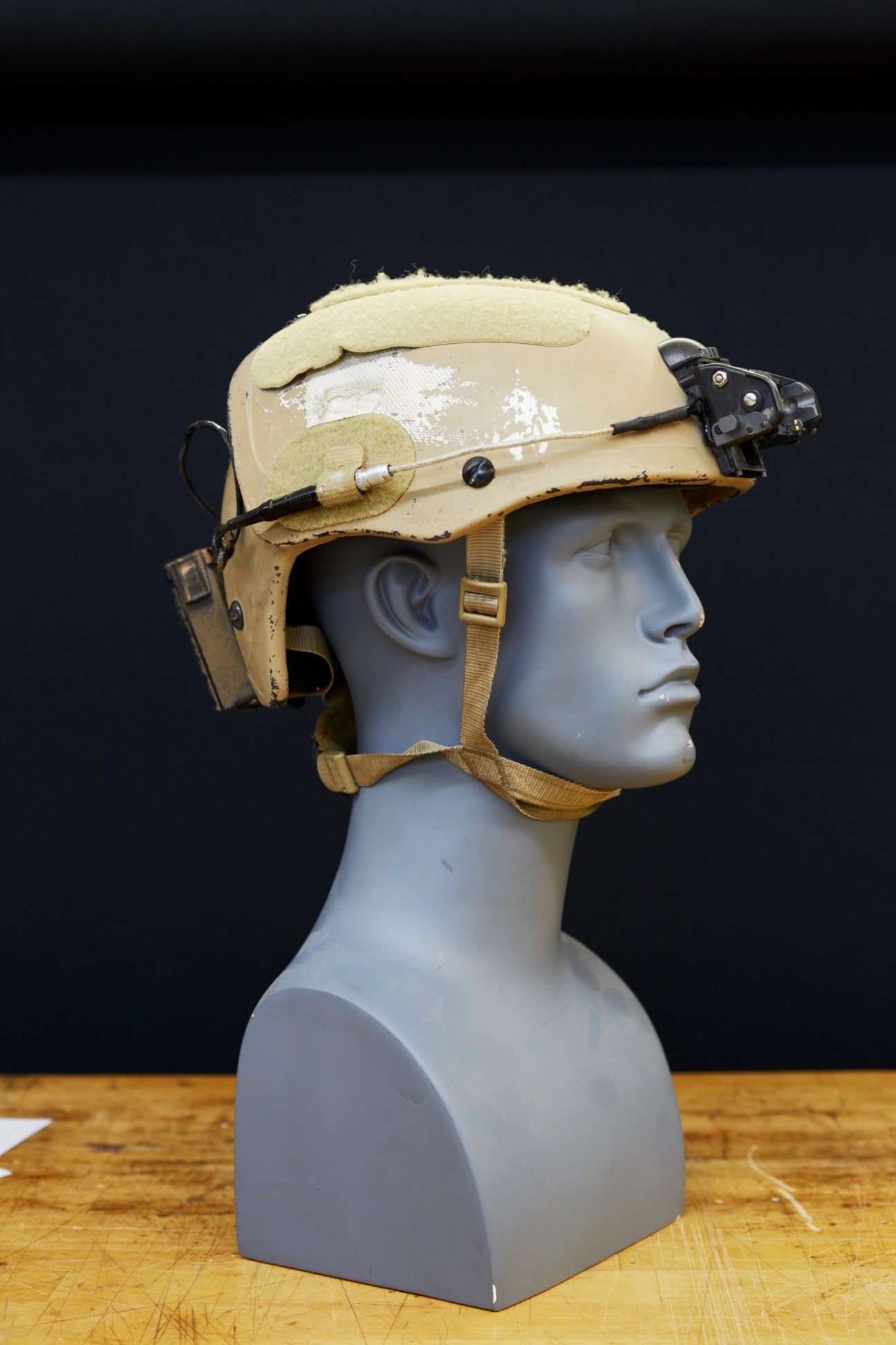 Tan combat helmet on mannequin head showing bullet deflection damage on crown