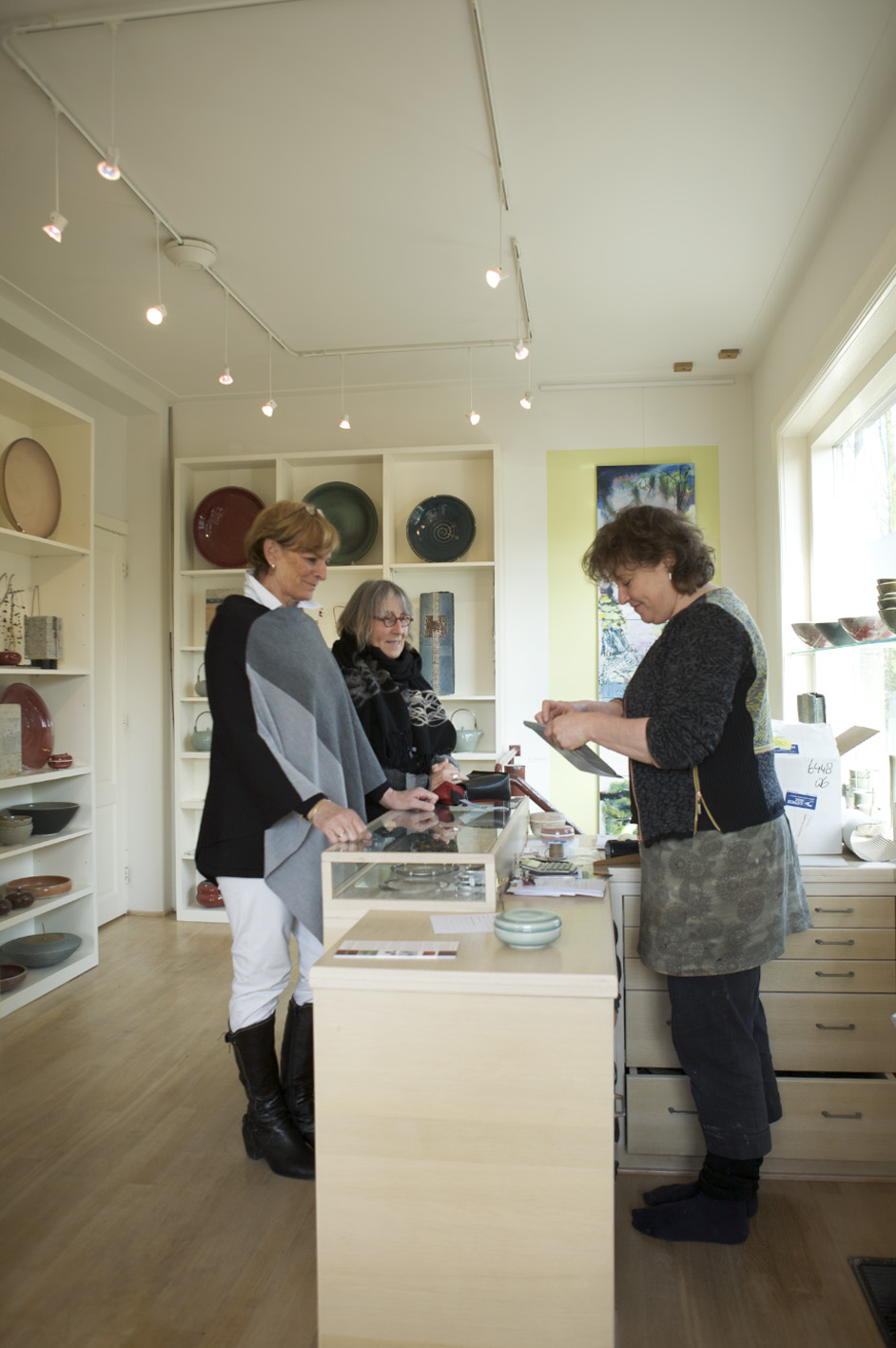 Marjoke De Heer ceramics shop interior with customers browsing handcrafted pottery displayed on white shelving.