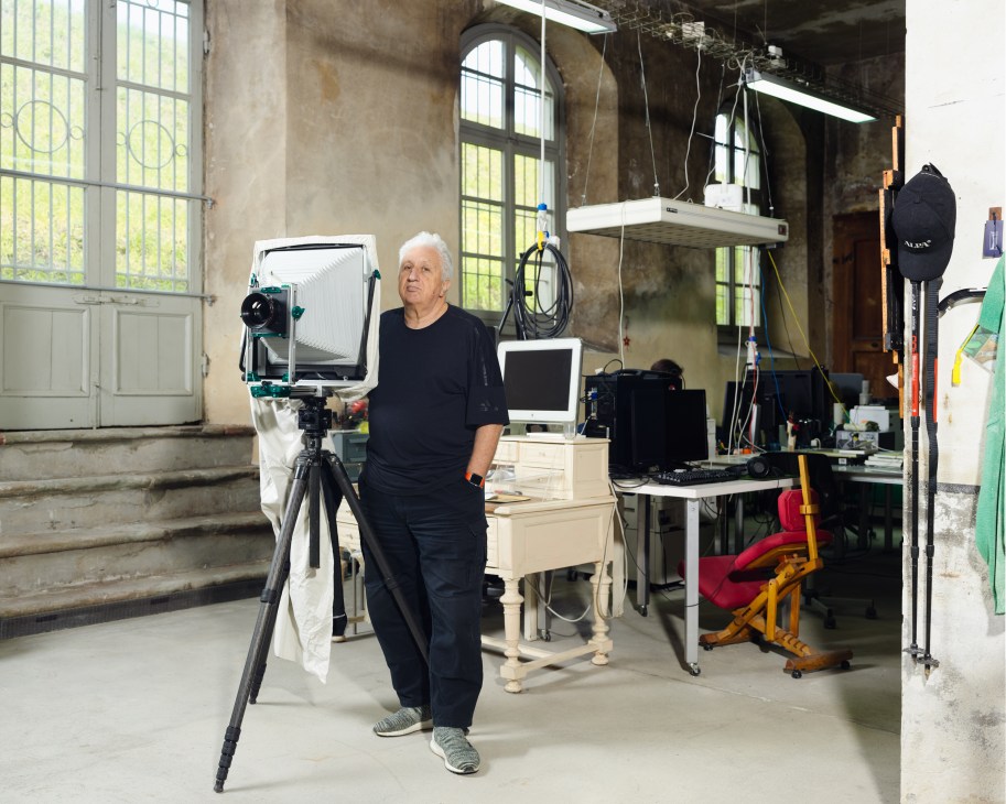 Massimo Vitali stands in his studio next to a large-format camera mounted on a tripod.