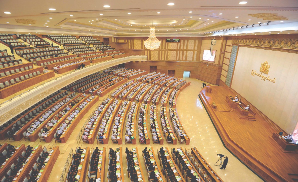 Members of parliament seated in curved rows within the grand wooden chamber of the Union Parliament in Naypyidaw.