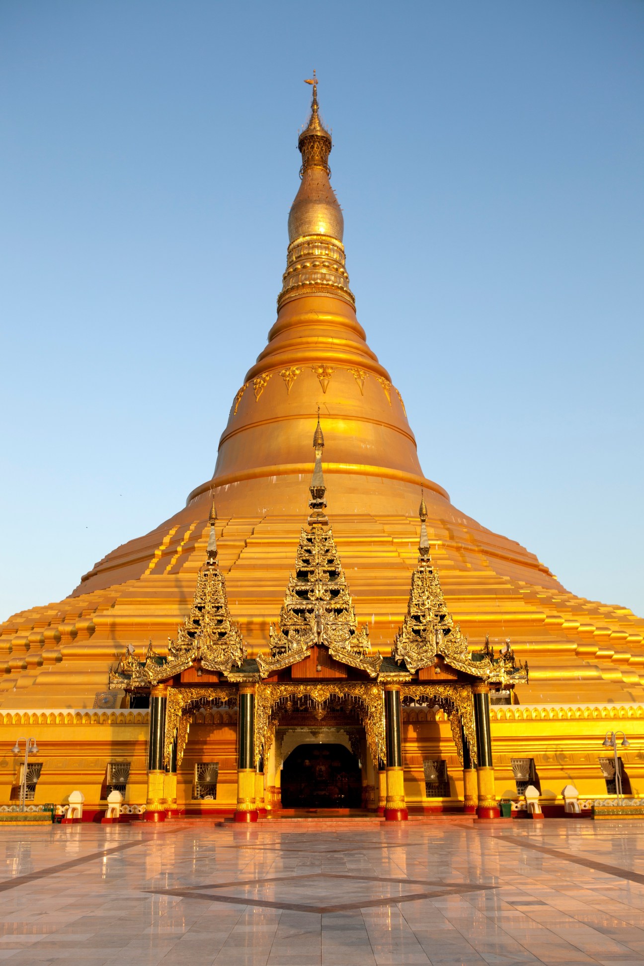 Golden pagoda with ornate spire and decorated entrance pavilion against blue sky in Naypyidaw