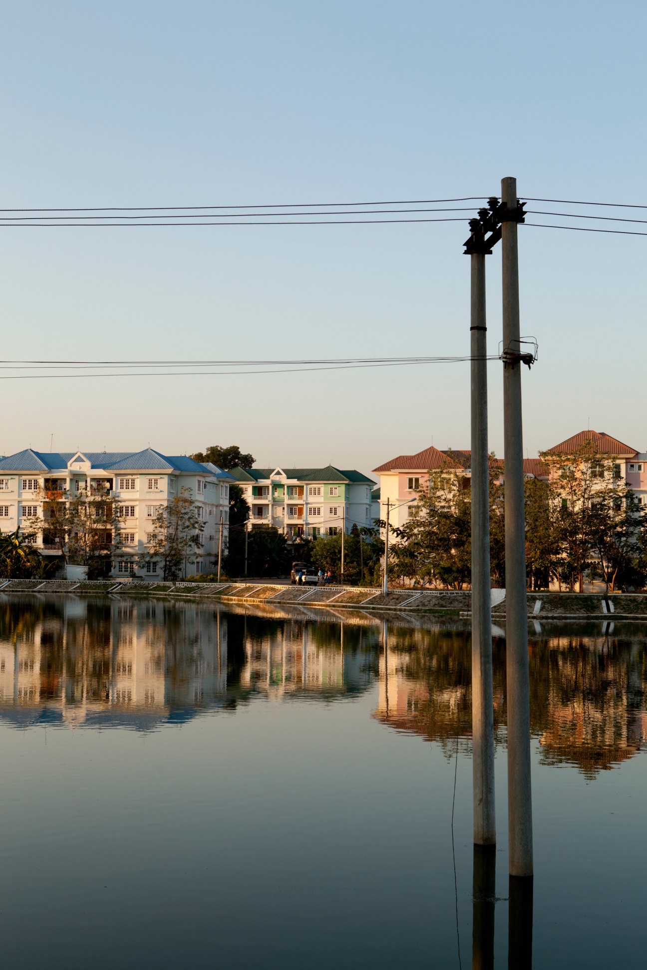 Colorful apartment buildings reflected in still water with utility pole in foreground in Naypyidaw.