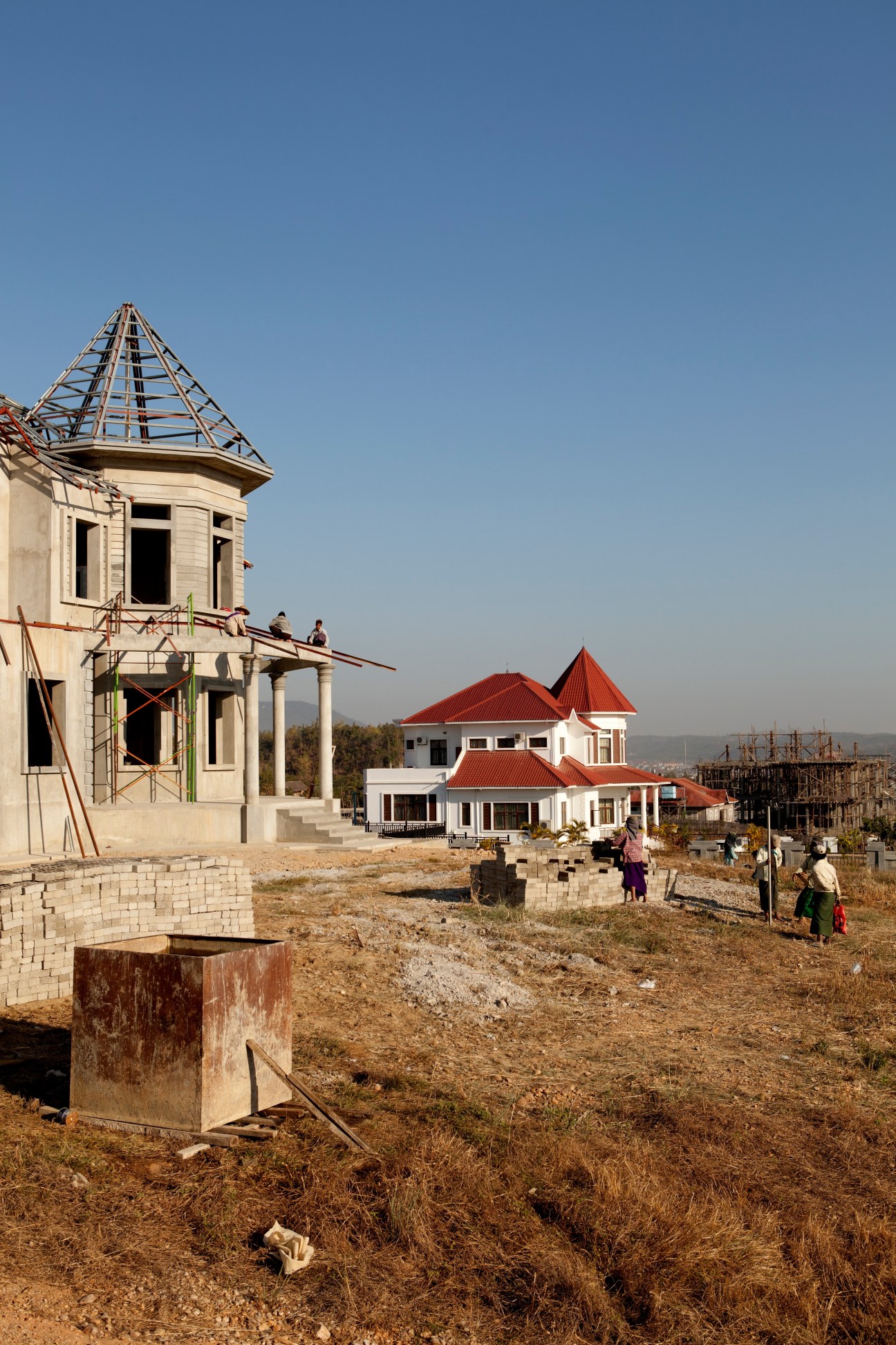 Houses under construction in Oake Taya Thiri district of Naypyidaw with cream and red-roofed structures on bare earth.