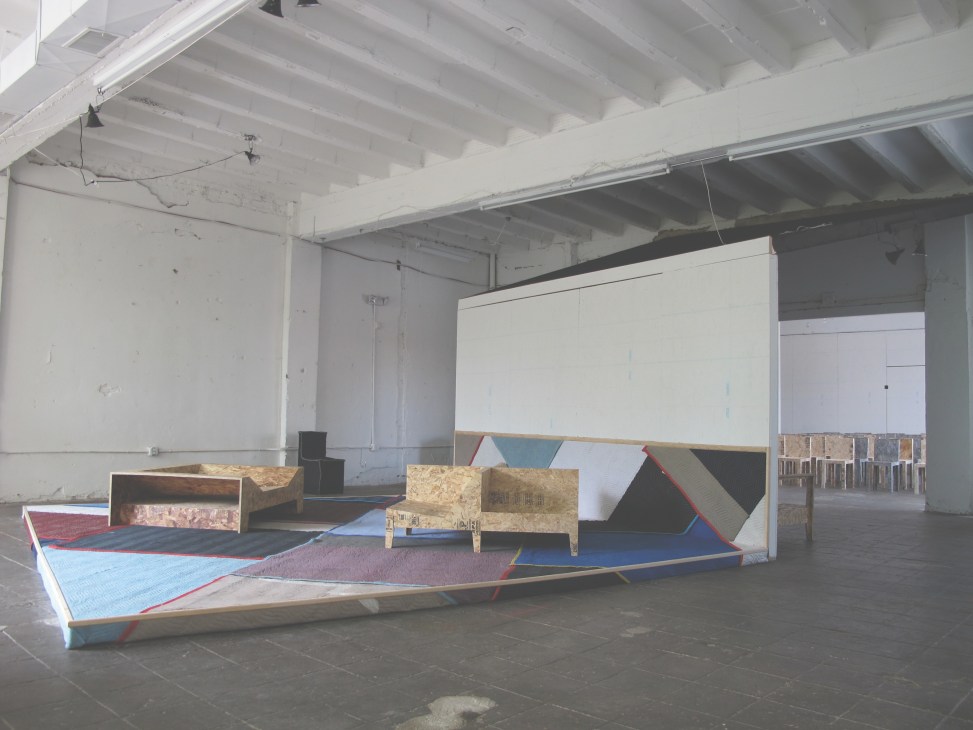 Industrial gallery space with contemporary furniture design installations featuring geometric pieces and colorful textiles.