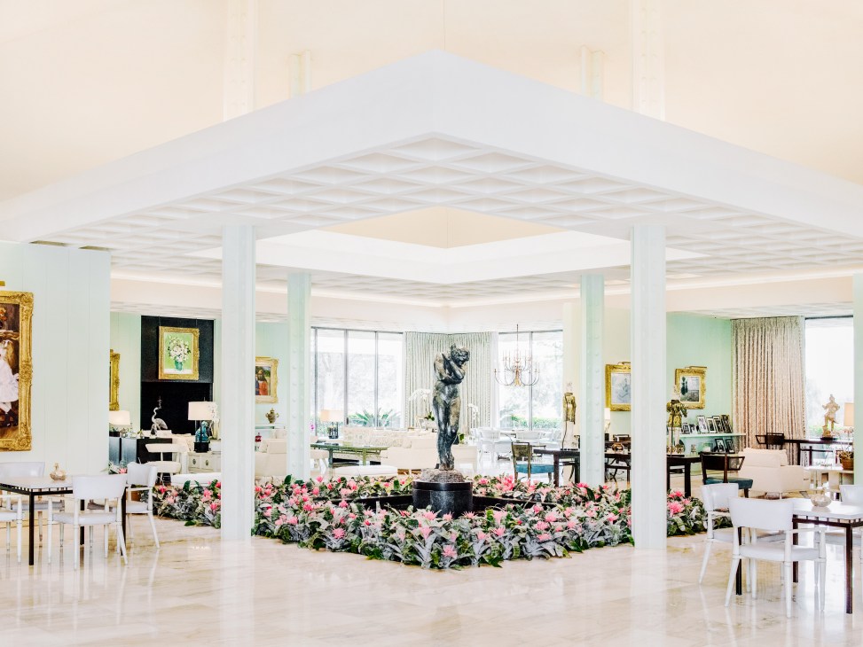 Spacious mid-century modern interior at Sunnylands with soaring ceilings, white columns, and pink flowers surrounding a dark sculpture.