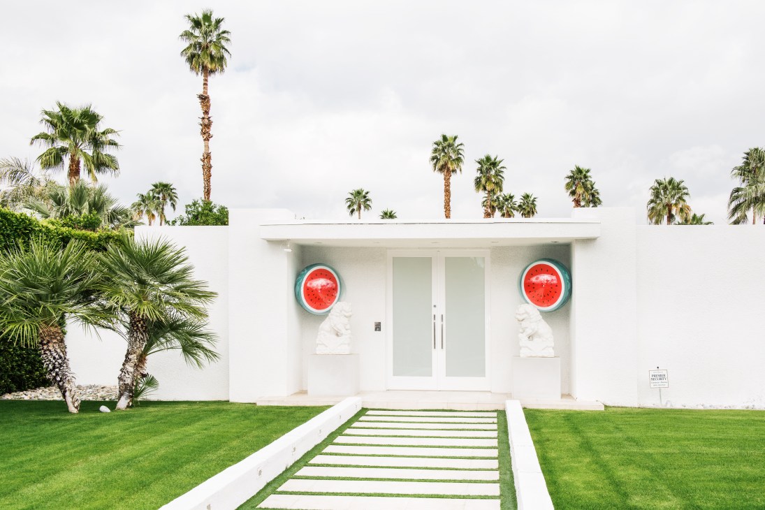 White mid-century modern house with red grapefruit-themed circular wall art and white sculptural busts flanking the entrance.