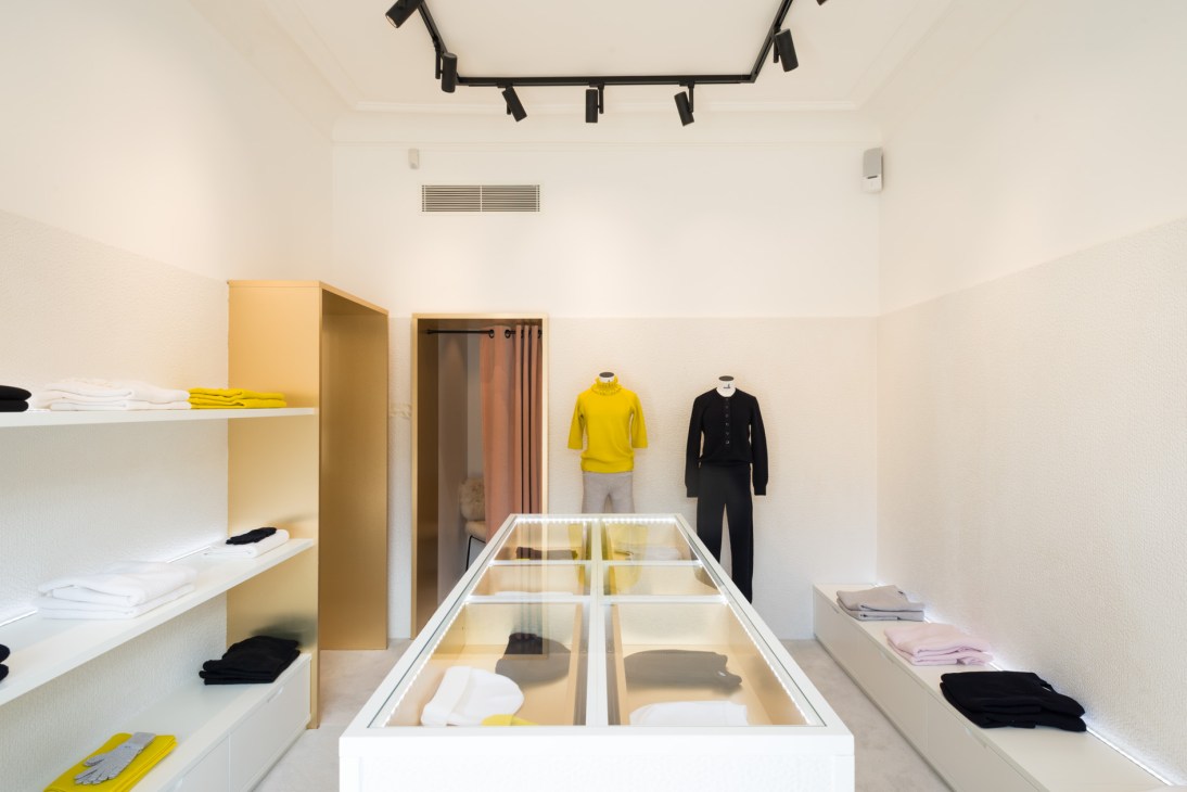 Interior of Molli shop with minimalist white display cases, shelving, and two mannequins wearing yellow and black clothing on Boulevard Saint-Germain.