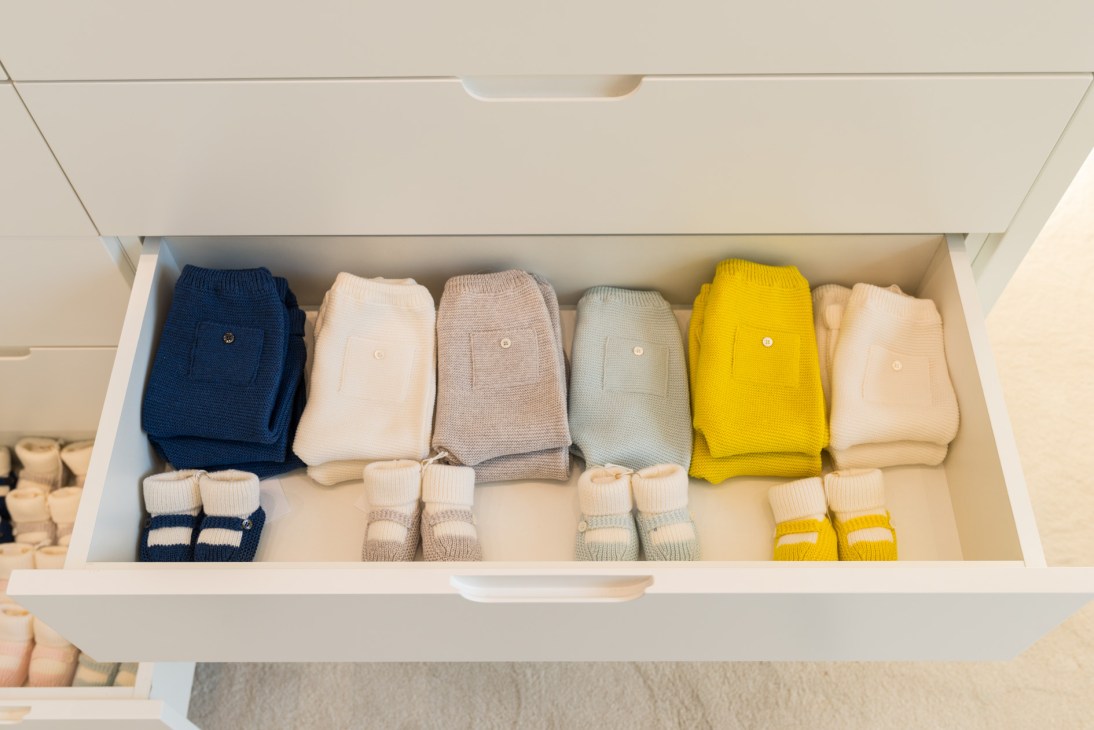 Drawer of neatly folded Molli baby clothes in pastel and bright colors including navy, cream, taupe, sage, and yellow.