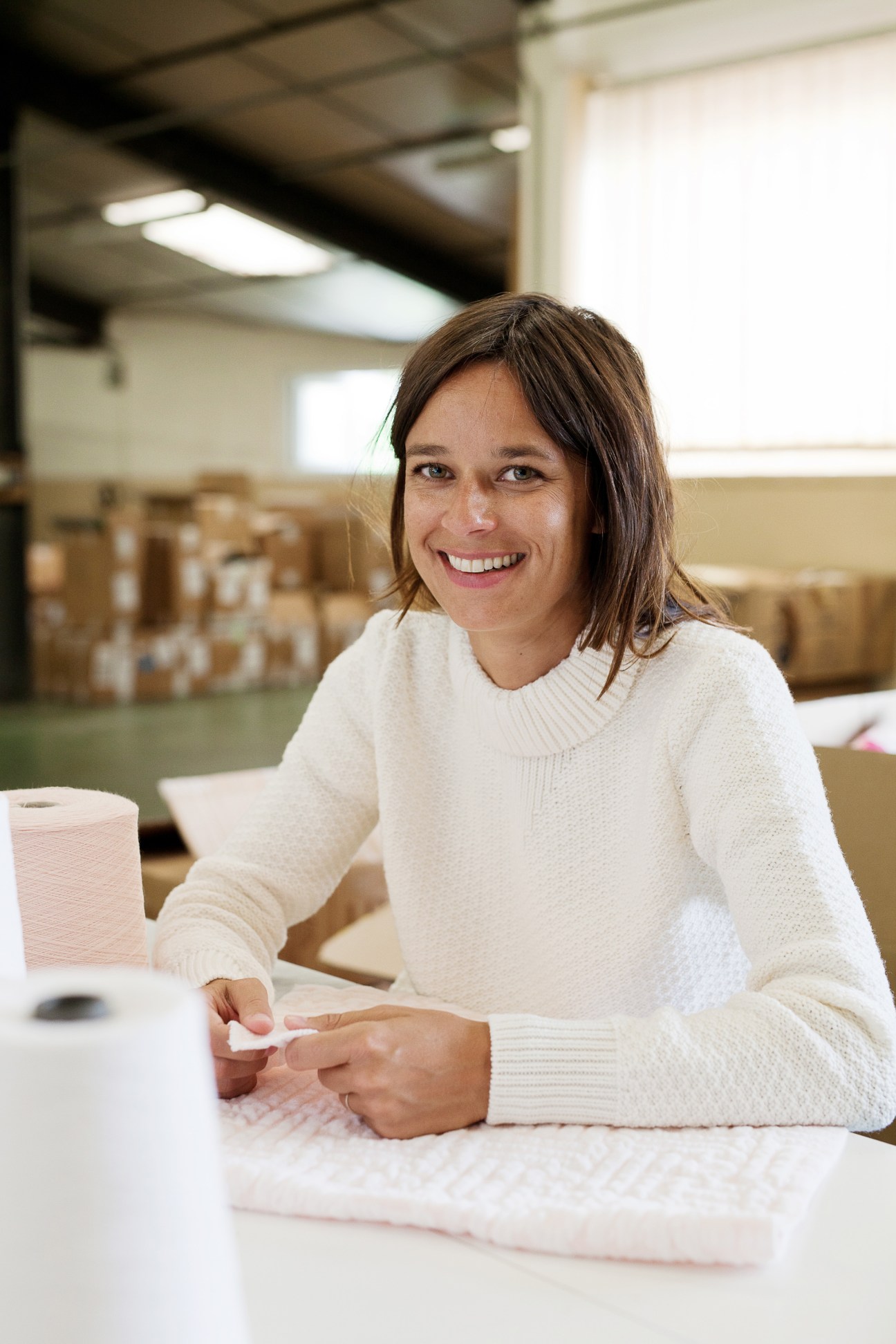 Charlotte de Fayet, owner of Molli childrenswear brand, smiling at a table in a factory setting.