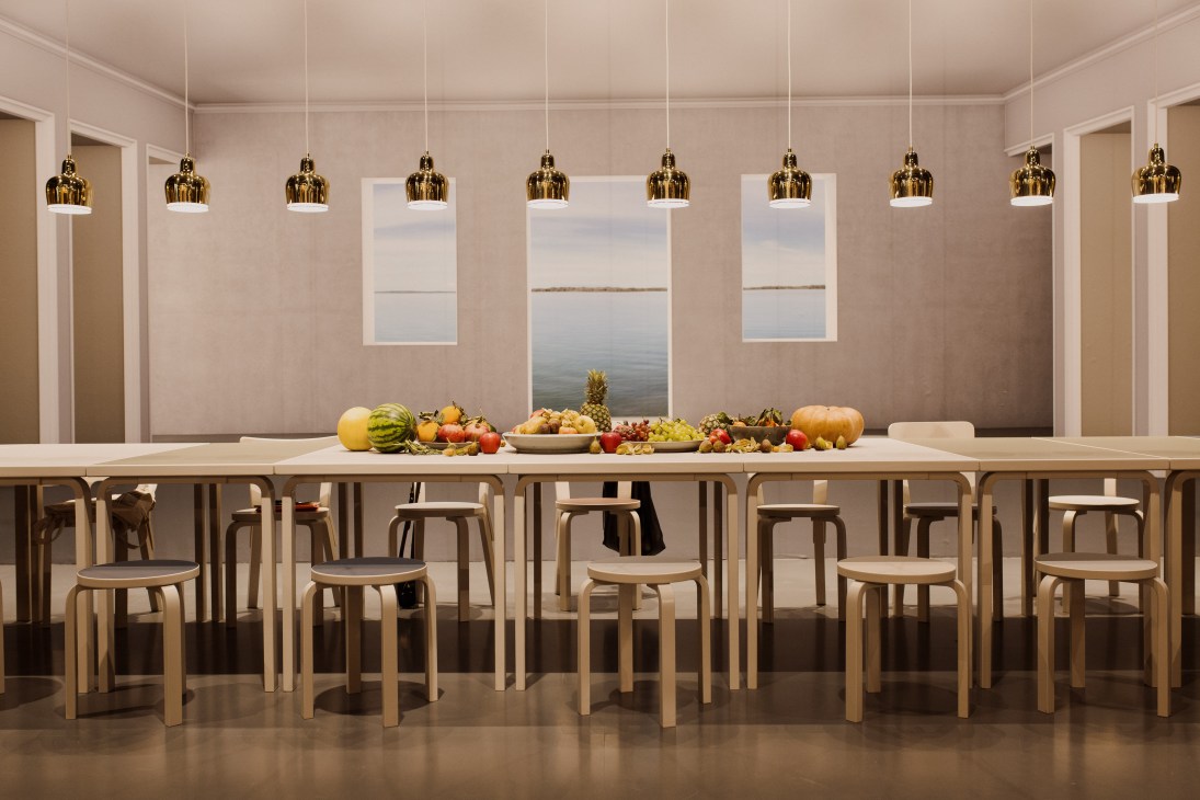Modern dining room display with wooden table, chairs, gold pendant lights and fresh produce.