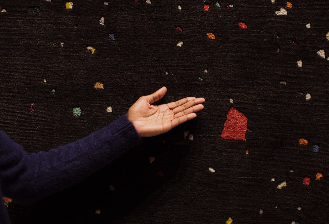 Hand resting on a black rug with colorful geometric patterns scattered across it.