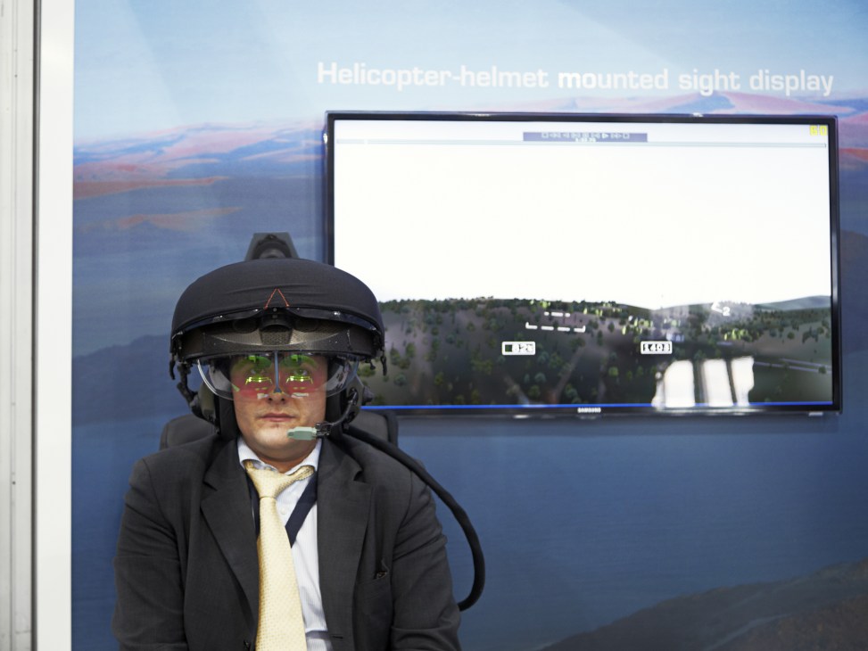 Delegate wearing BAE Systems Striker helmet with mounted sight display showing aerial landscape overlay.