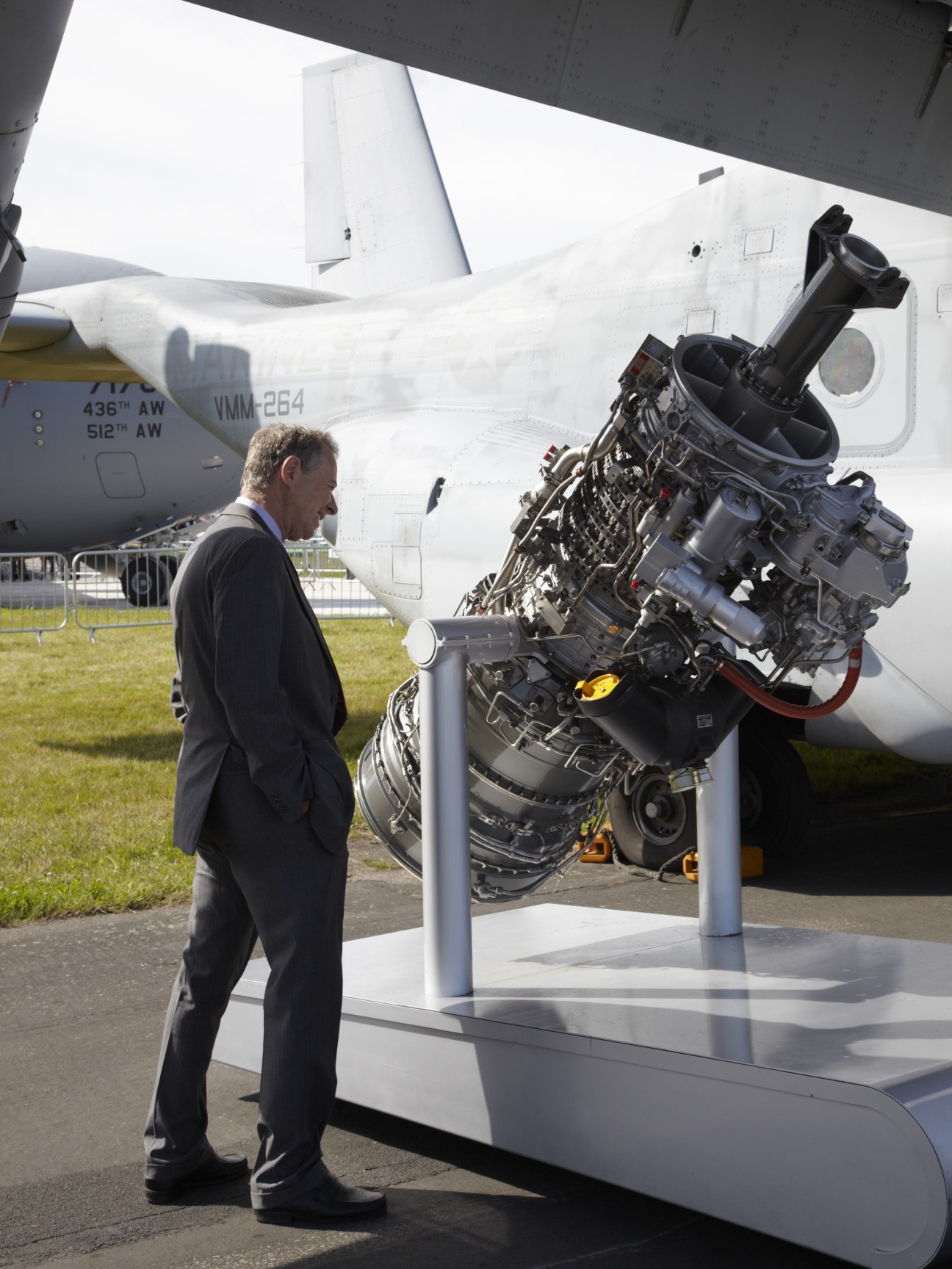 Man in business suit examining a large Rolls-Royce aircraft engine on display at an air show.