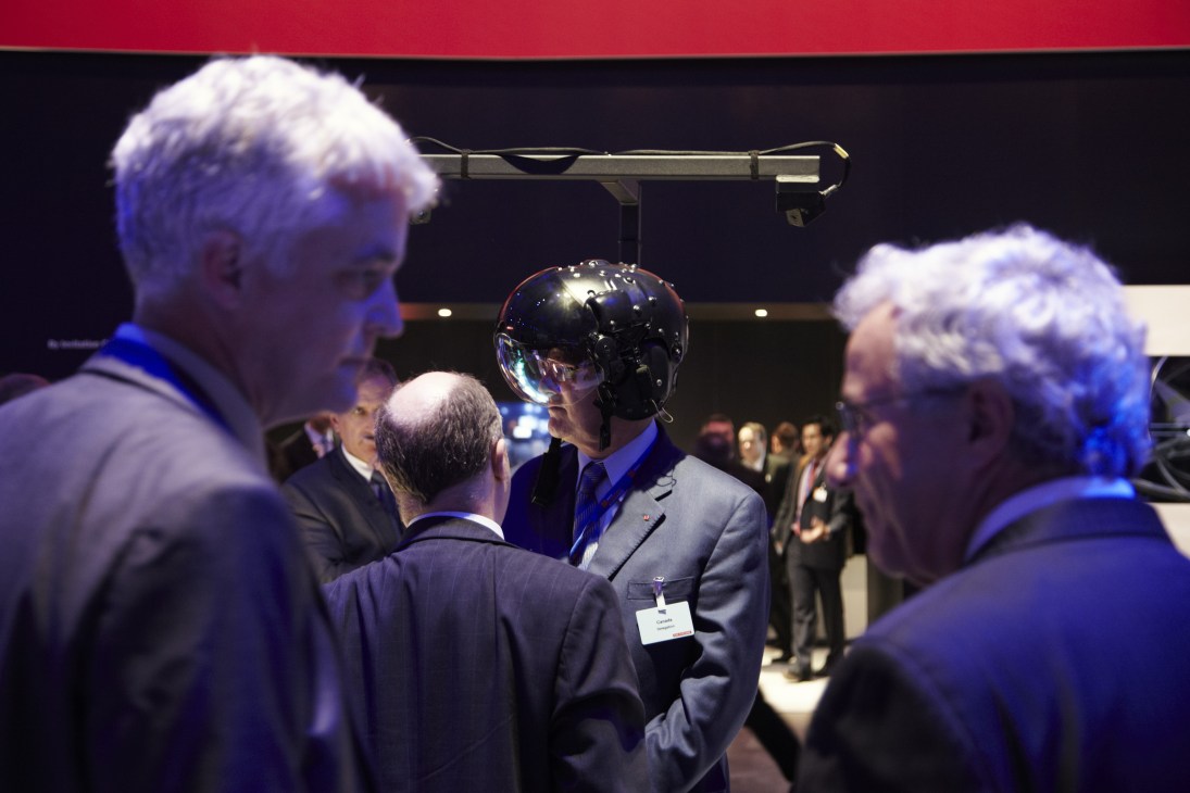 Delegates in business attire examine a black BAE Systems Striker helmet displayed at the Farnborough air show.