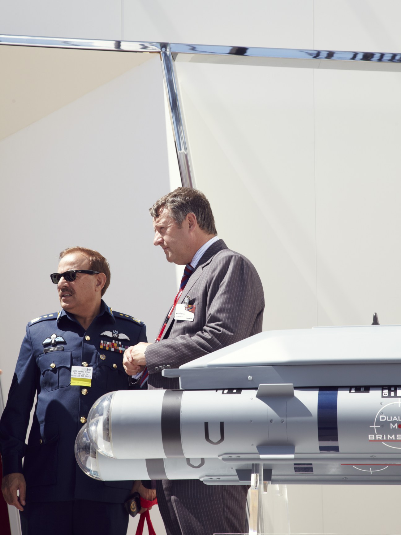 Pakistan Air Force official in blue uniform and businessman examining a Brimstone missile system at Farnborough Air Show.